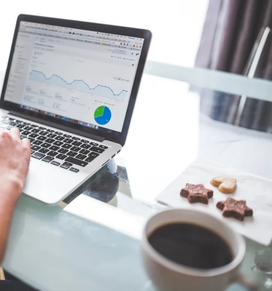 Análise de Campanhas de Tráfego Pago na Incentiva+ Consulting num computador numa secretária com cookies e café ao lado